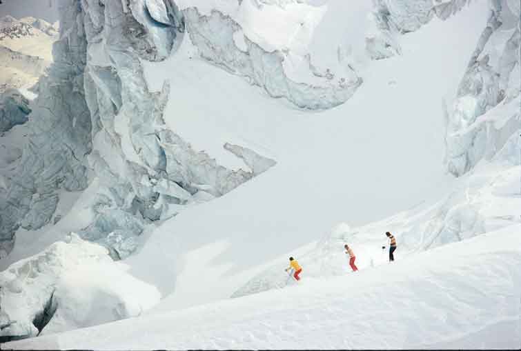 Three skiers under a large glacier. Historical 1981 photo courtesy of CMH Heli-Skiing & Summer Adventures