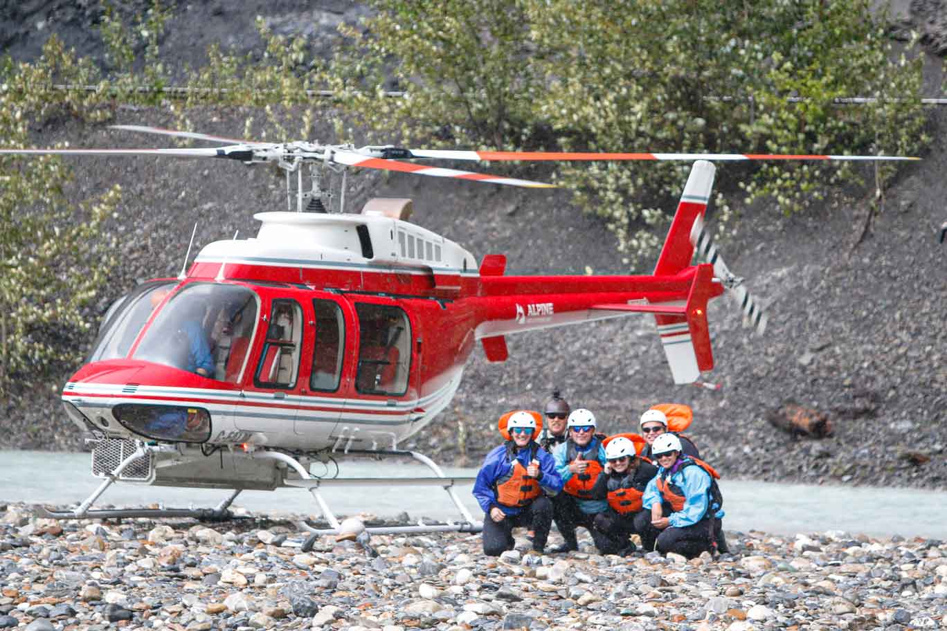 A group of rafters crouch near a helicopter, awaiting transport to the next section of river