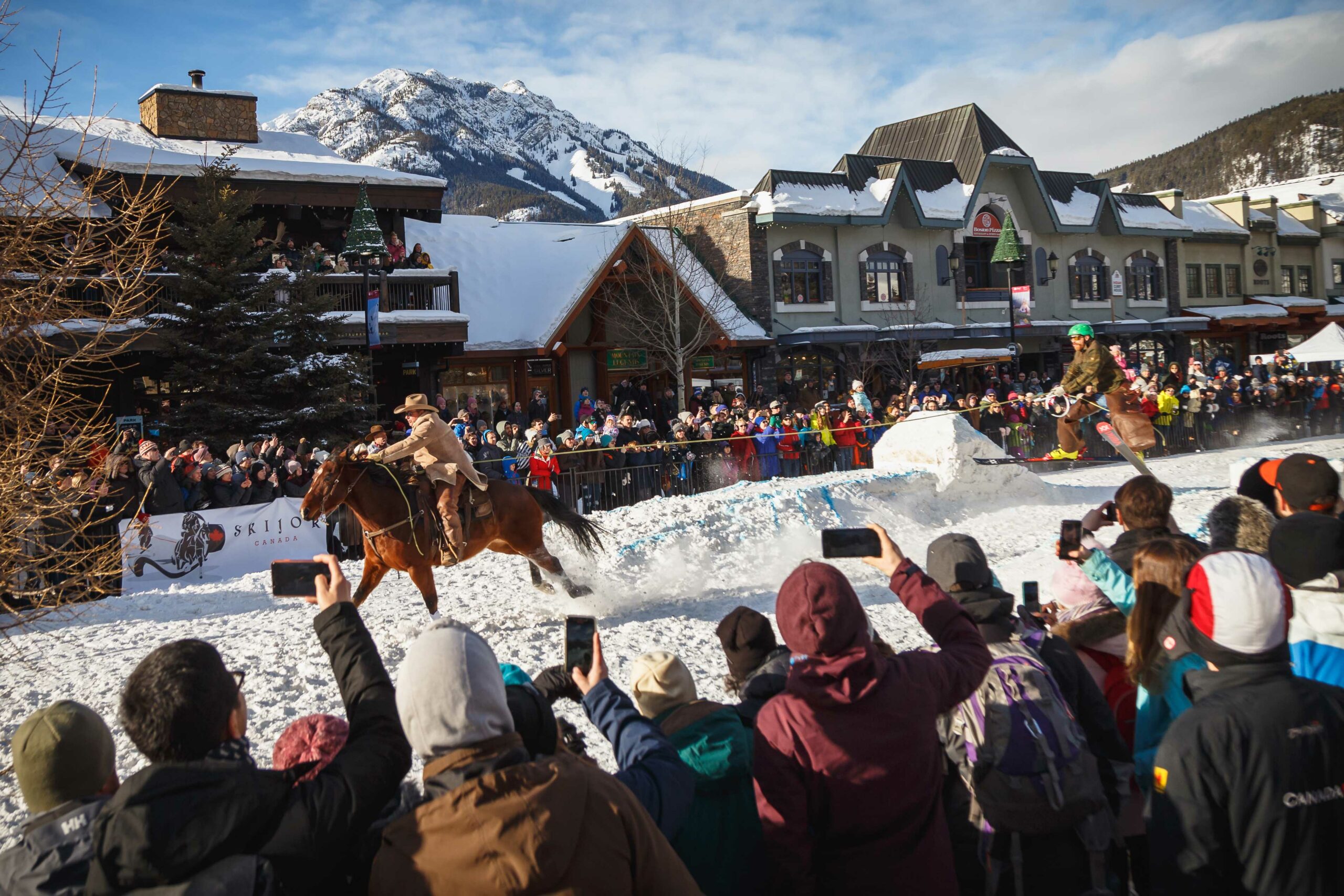 A horse gallops down Main Street in Banff pulling a trick skier in front of a crowd during SnowDays