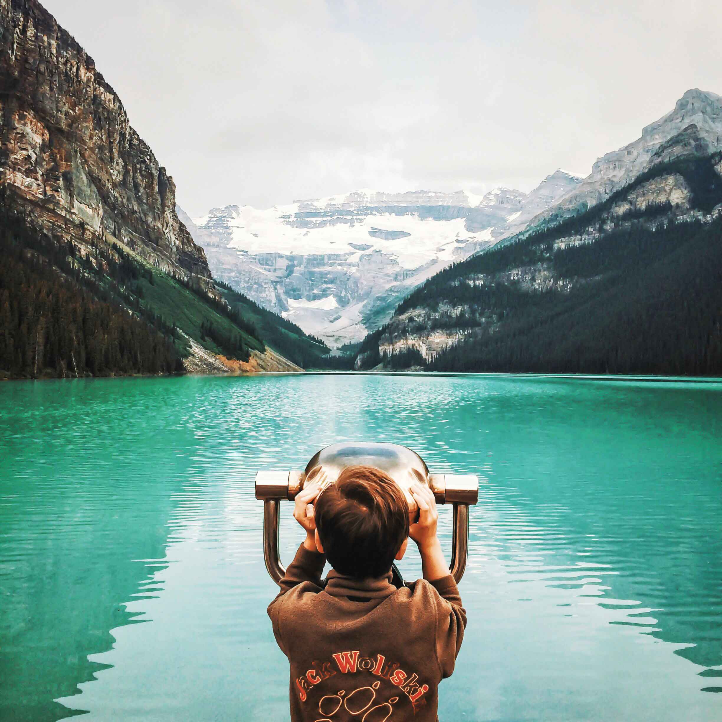 A young person looks through binoculars at the iconic Lake Louise