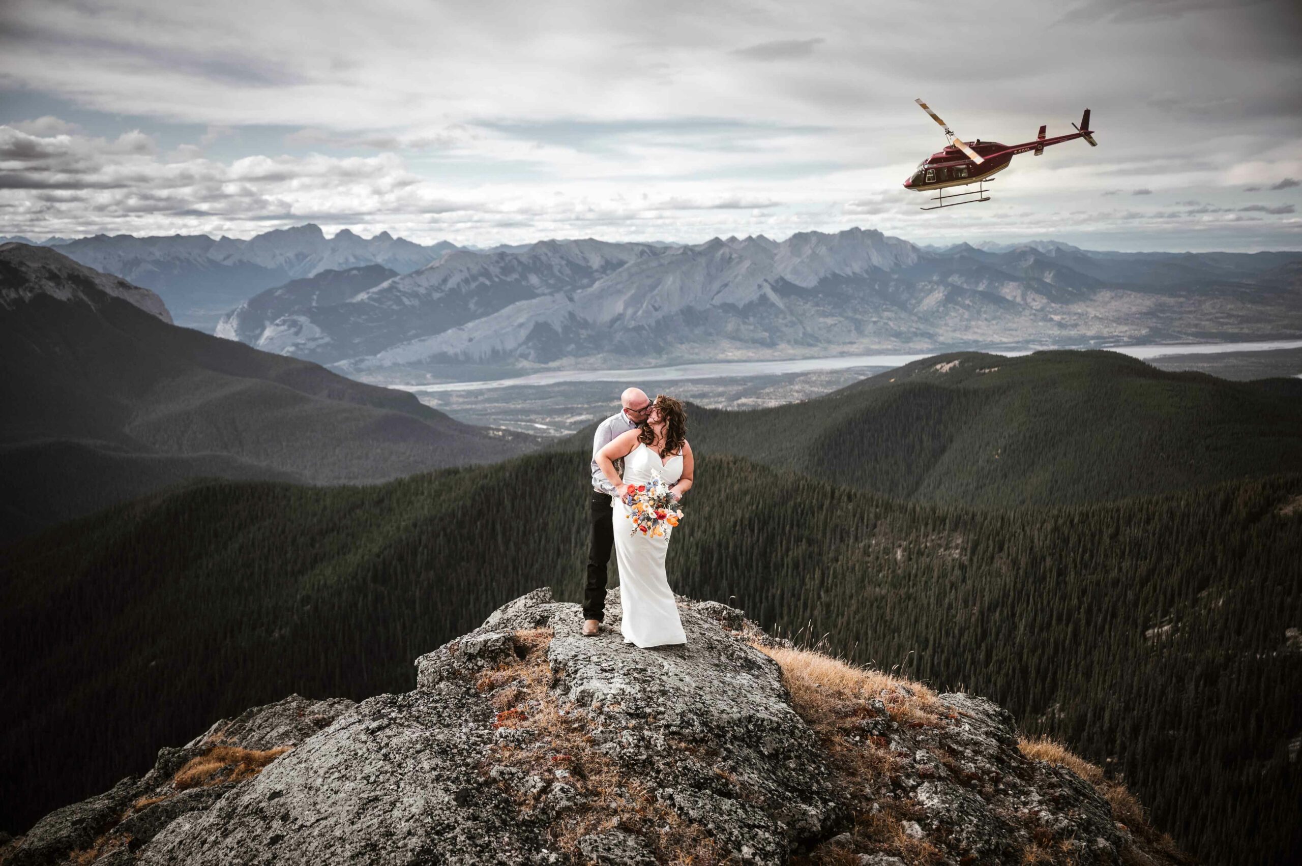 A couple getting married in the backcountry on a mountaintop with a helicopter in the background