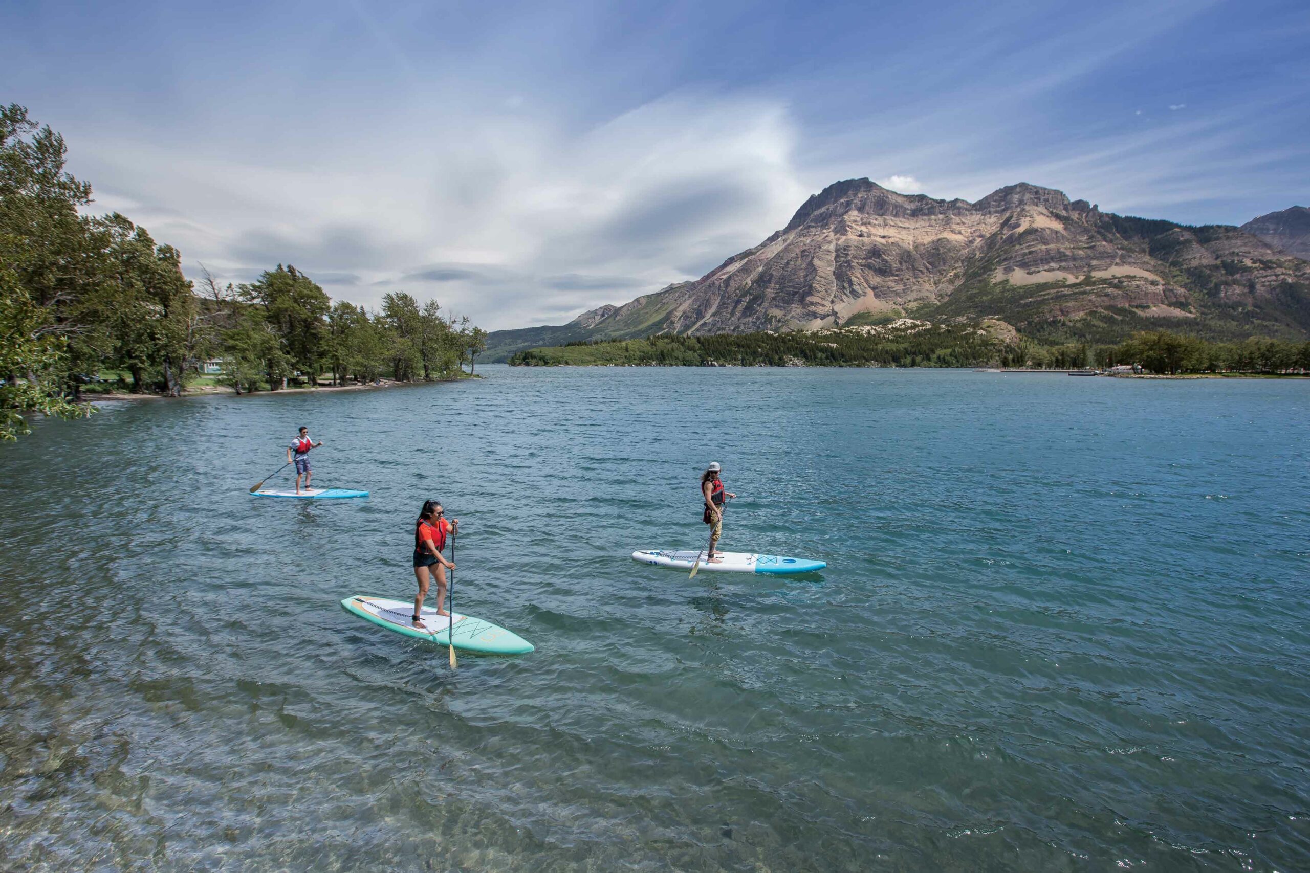 Three people paddleboard on a mountain ringed lake in Waterton Lakes National Park.