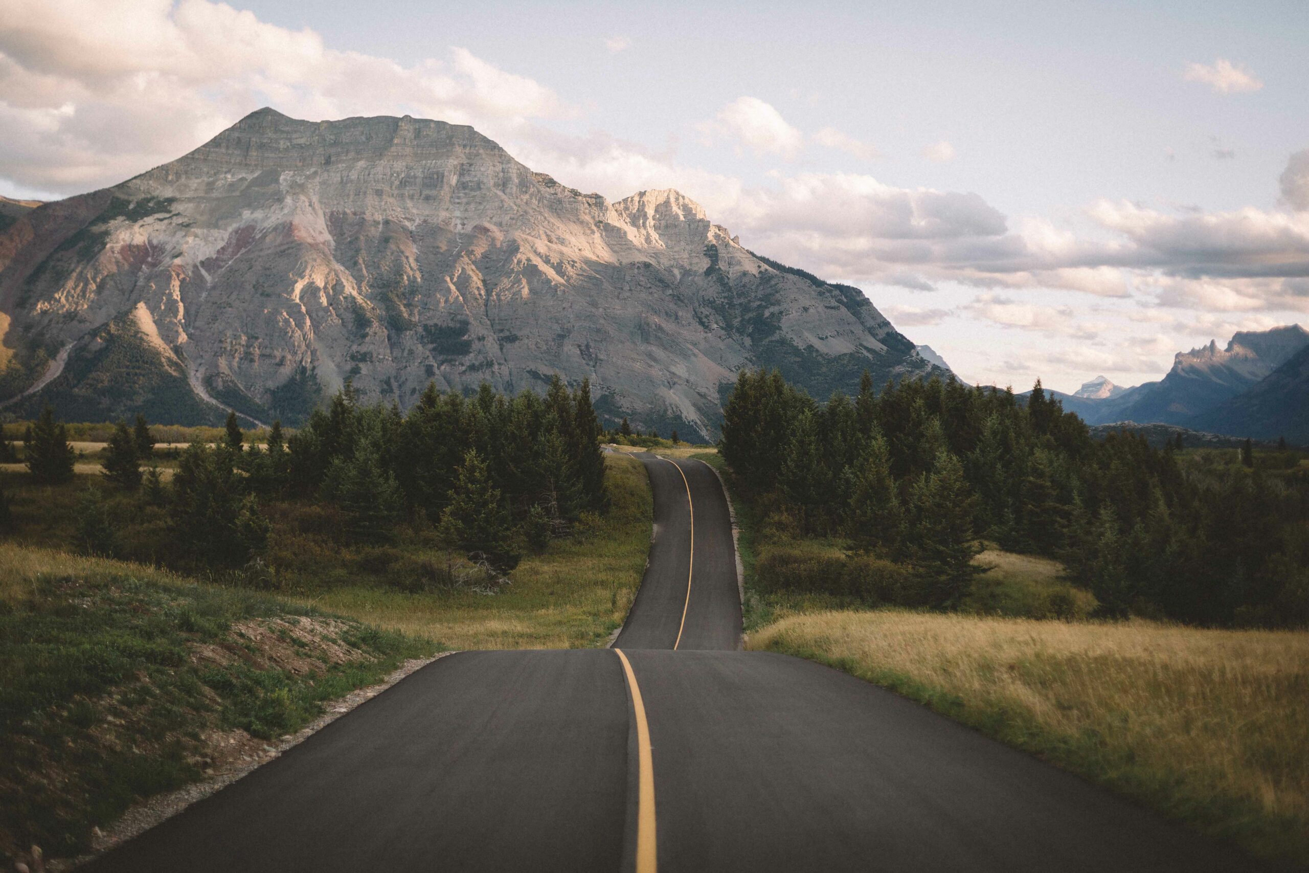 A winding road leads to the mountains to represent road trips in Waterton Lakes National Park.