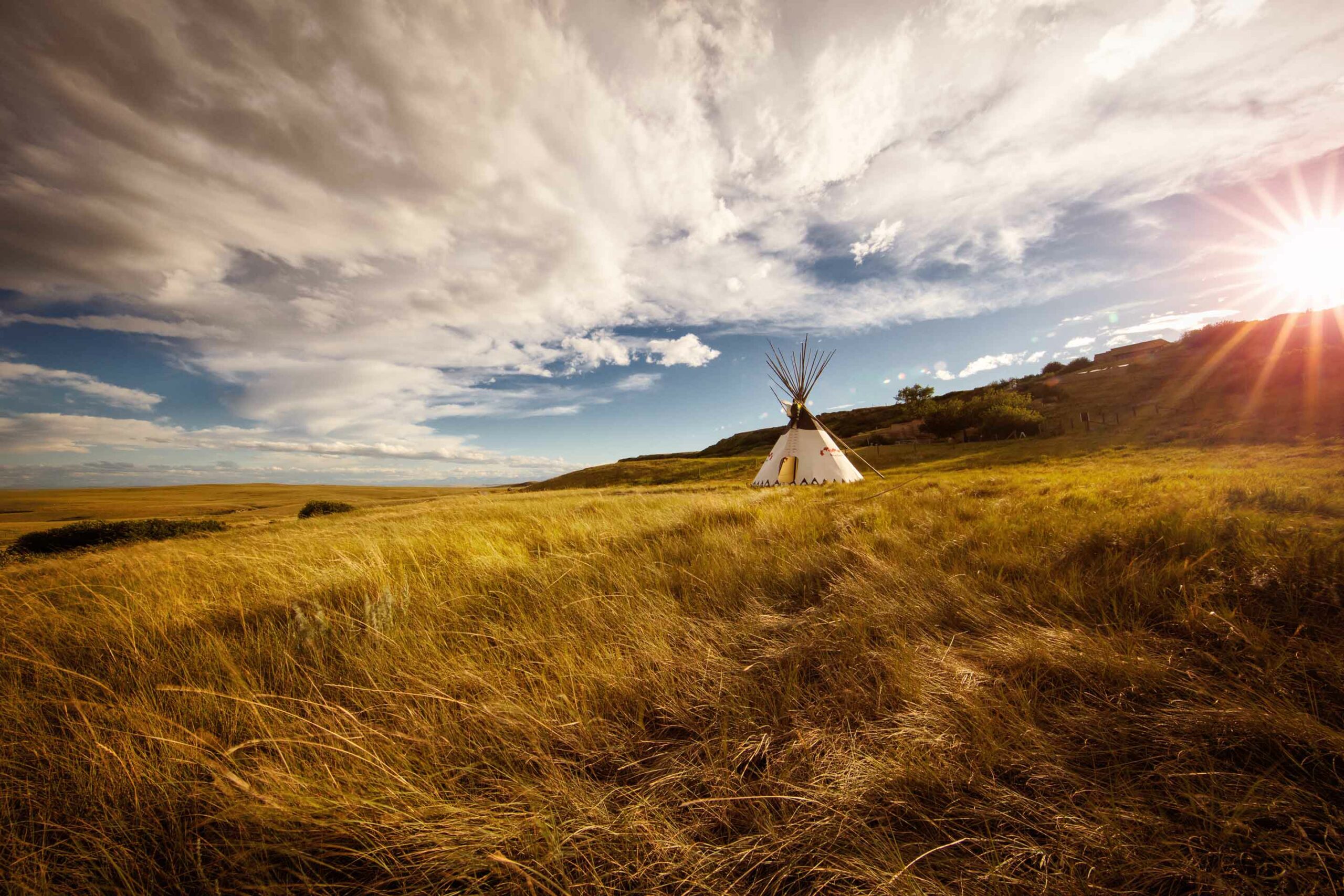Teepee in the middle of a field with cool clouds and sun peeking through at Head-Smashed-In Buffalo Jump in Southwestern Alberta