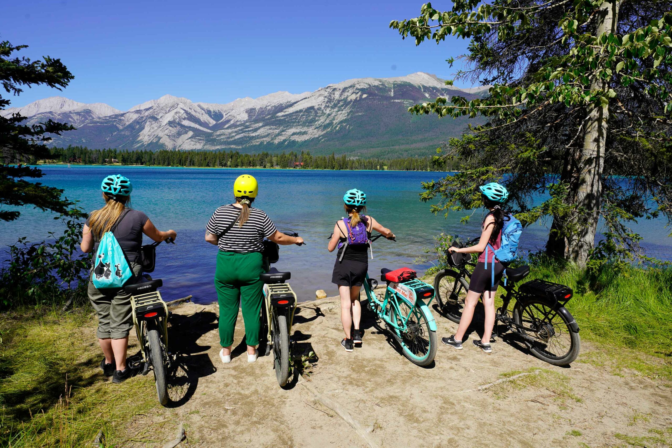 Four people with ebikes look over a scenic lake with a mountain in the background as part of the Bites on Ebikes tour with Jasper Food Tours