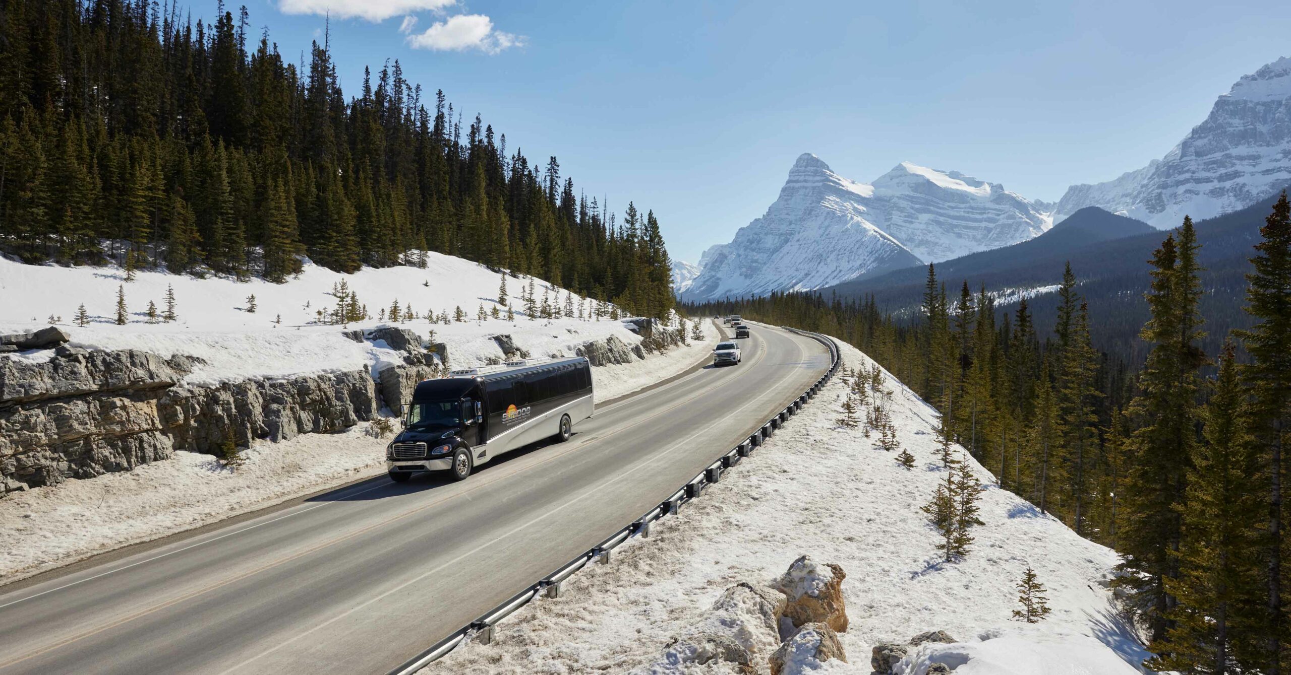 A transportation bus from Sundog Tours drives along a mountain road. If the weather isn't great for driving, consider taking transit as a winter driving safety alternative