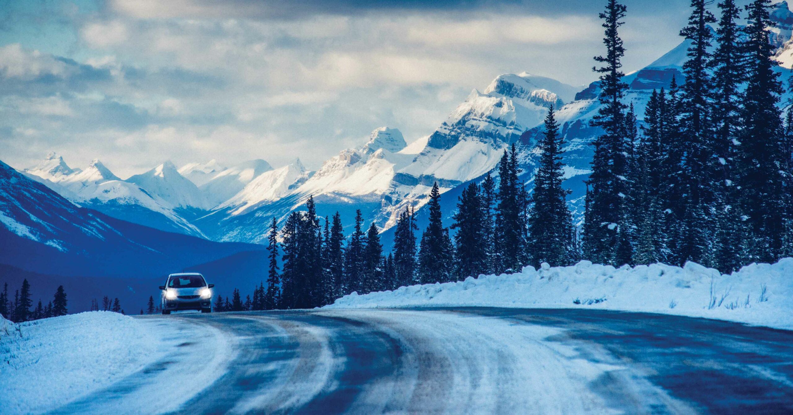 A car drives on centre bare roads in the winter in the mountains. Make sure to know the road conditions before you set out and practice winter driving safety