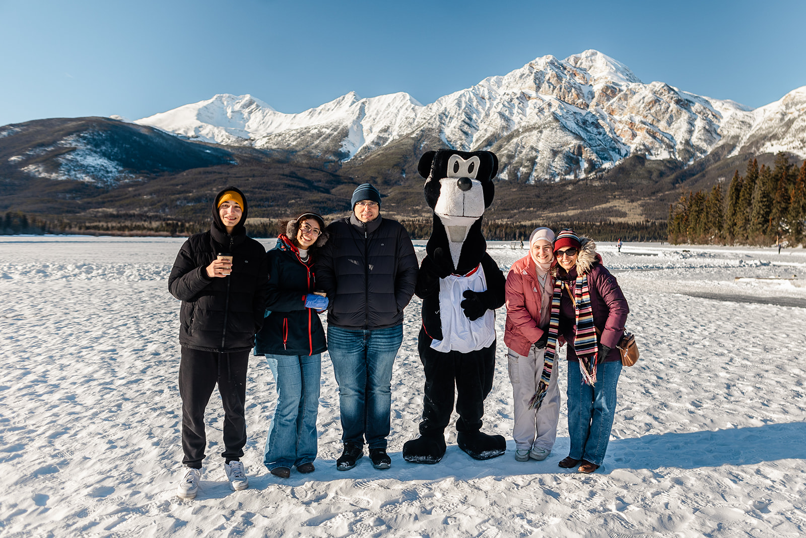 People stand with Jasper the Bear in front of mountains as part of the Jasper in January celebration.