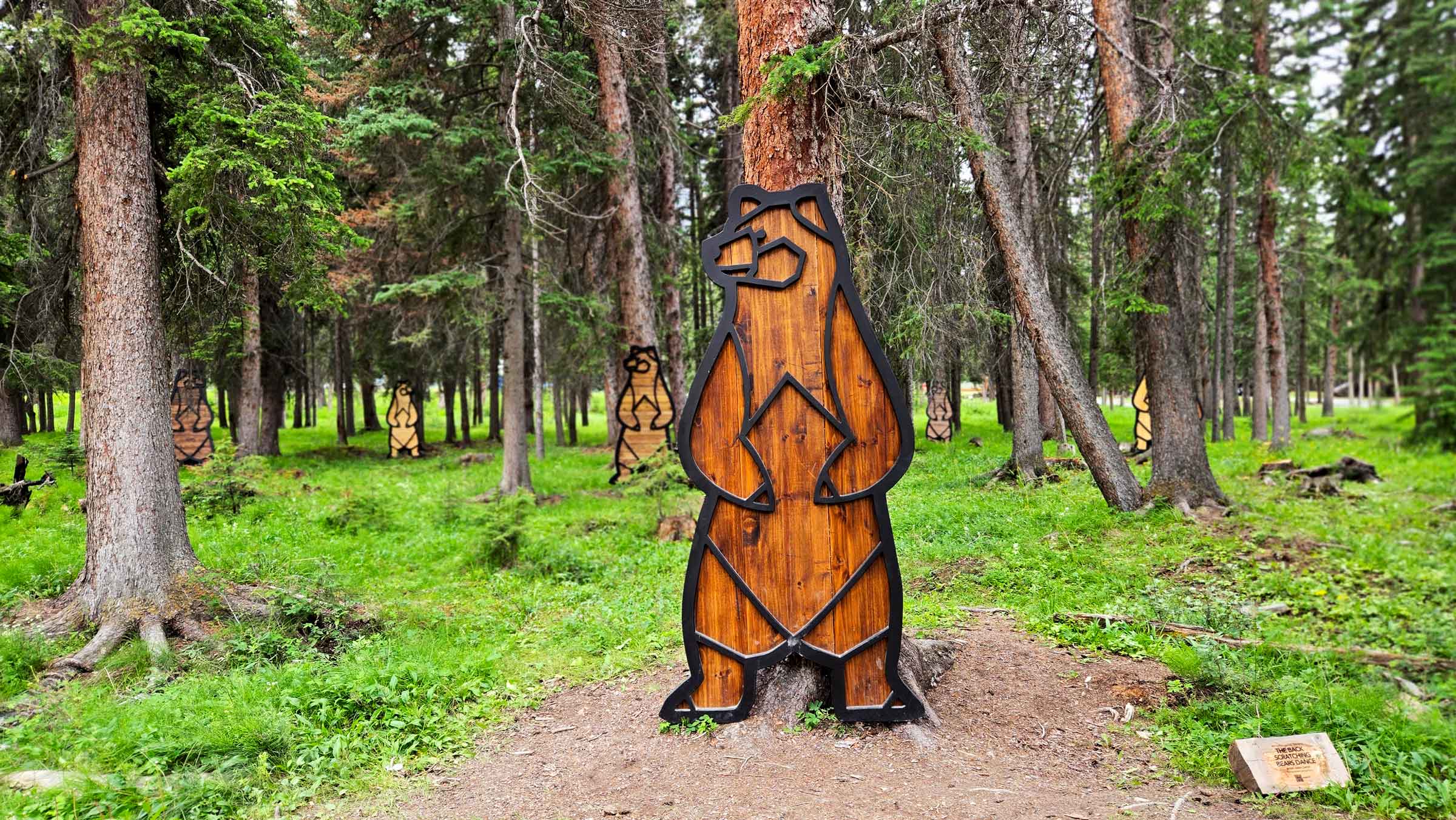 Wooden cutouts of bears appear to be scratching their backs on the trees in "The Back Scratching Bears Dance" by Jason Carter