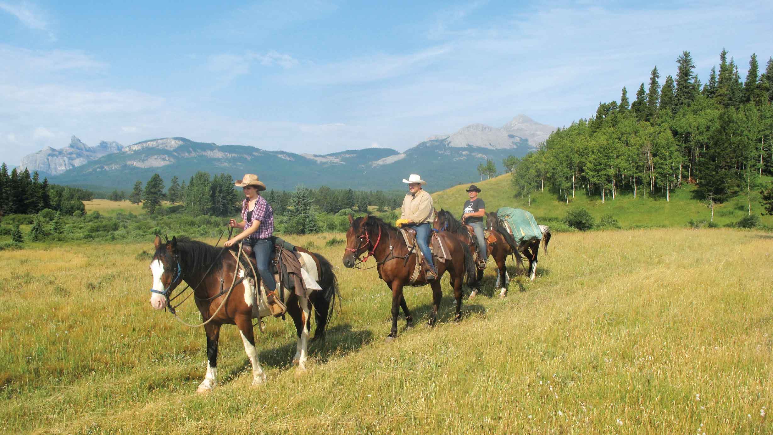 People ride through a field with mountains in the background with Brewster Adventures. 
