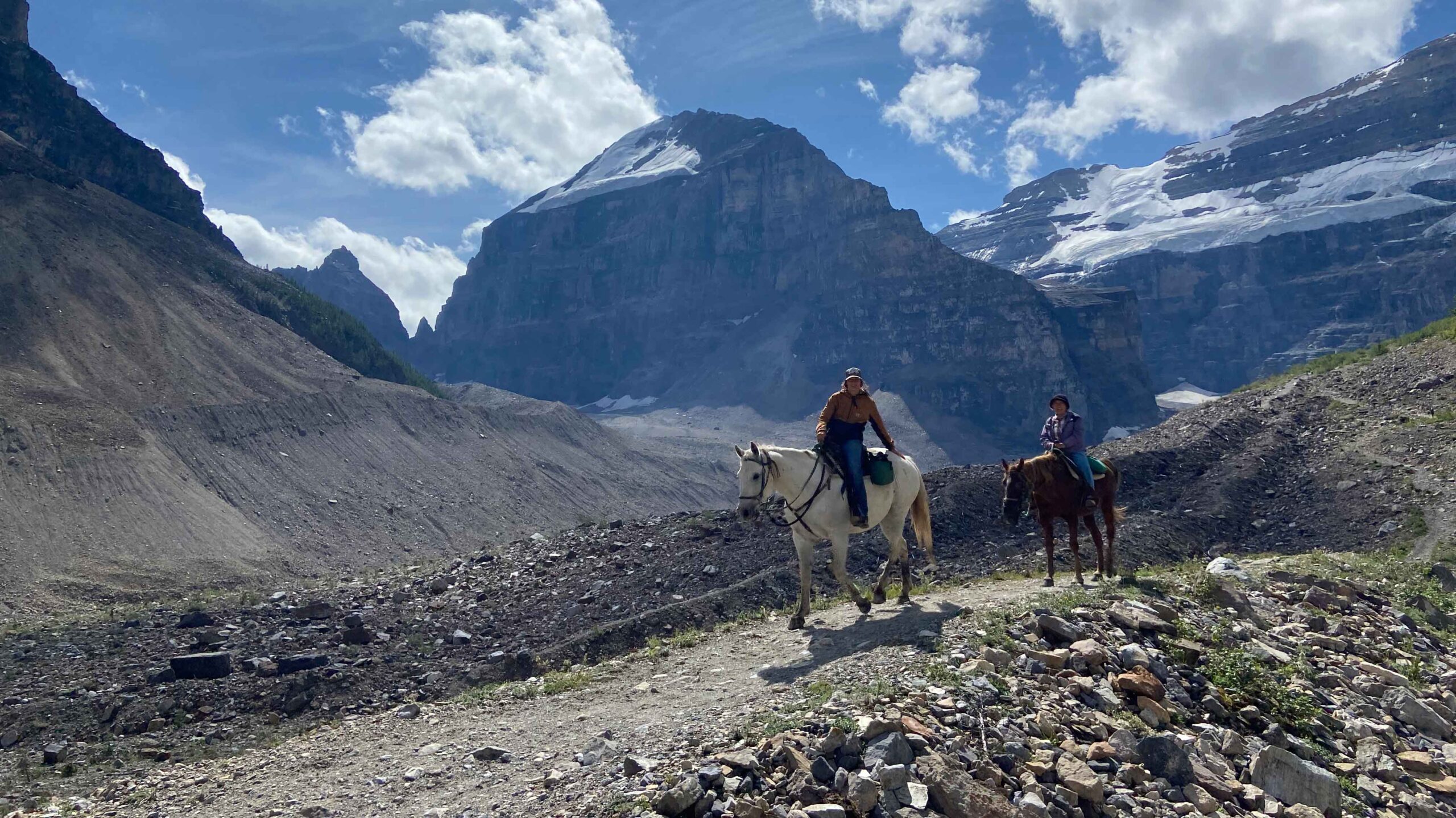 People live out their cowboy dreams and ride horses on a rocky trail with stunning mountains in the background
