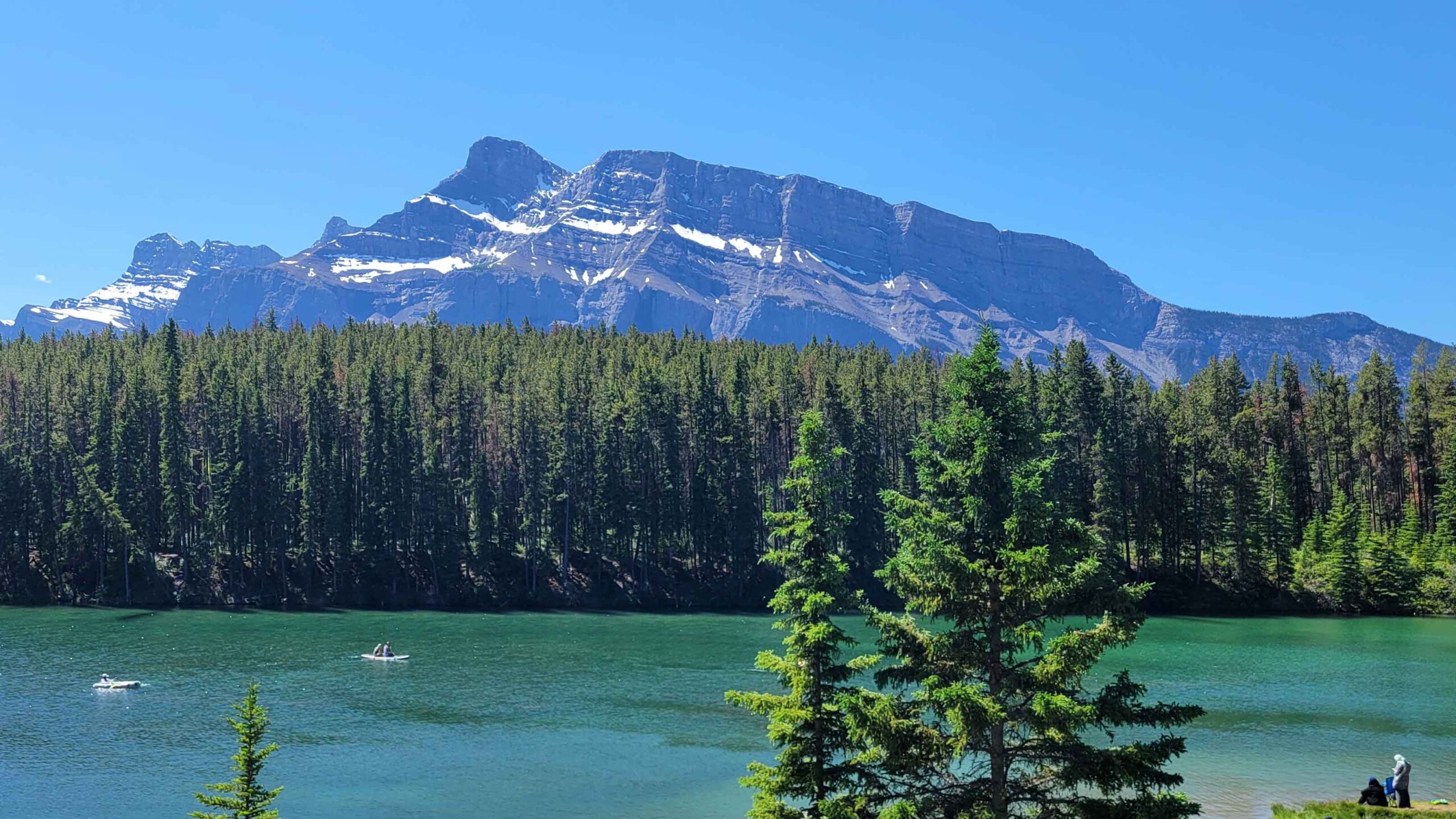 Paddle boarders and swimmers enjoy the warm-ish waters of Johnson Lake with an impressive Mount Rundle view in the background.