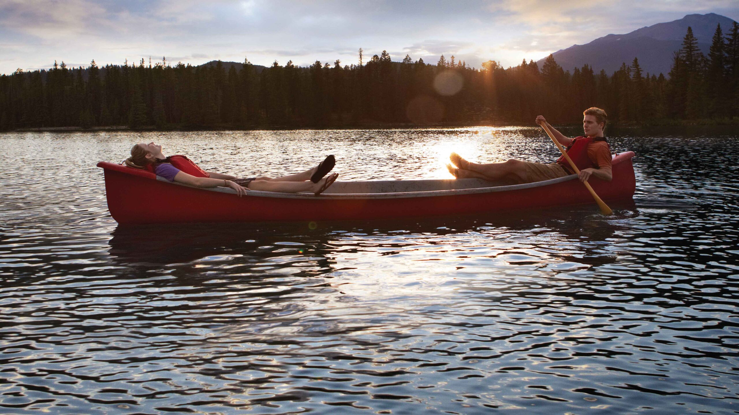 Two people relax in a red canoe at sunset on a lake. It's a great thing to do in Jasper this weekend