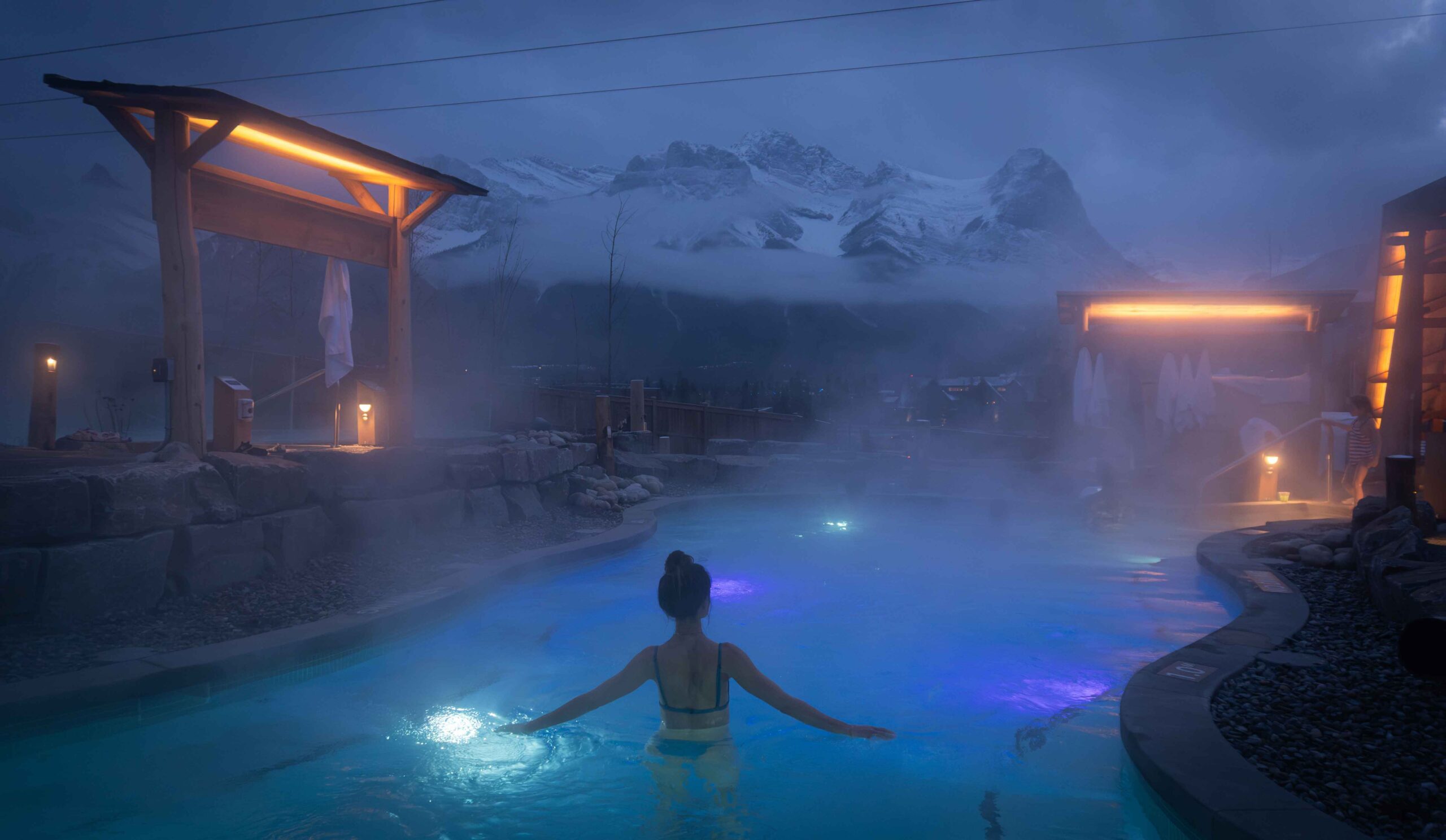 A person soaks in a hot pool at Everwild Sap with mountain views in the background