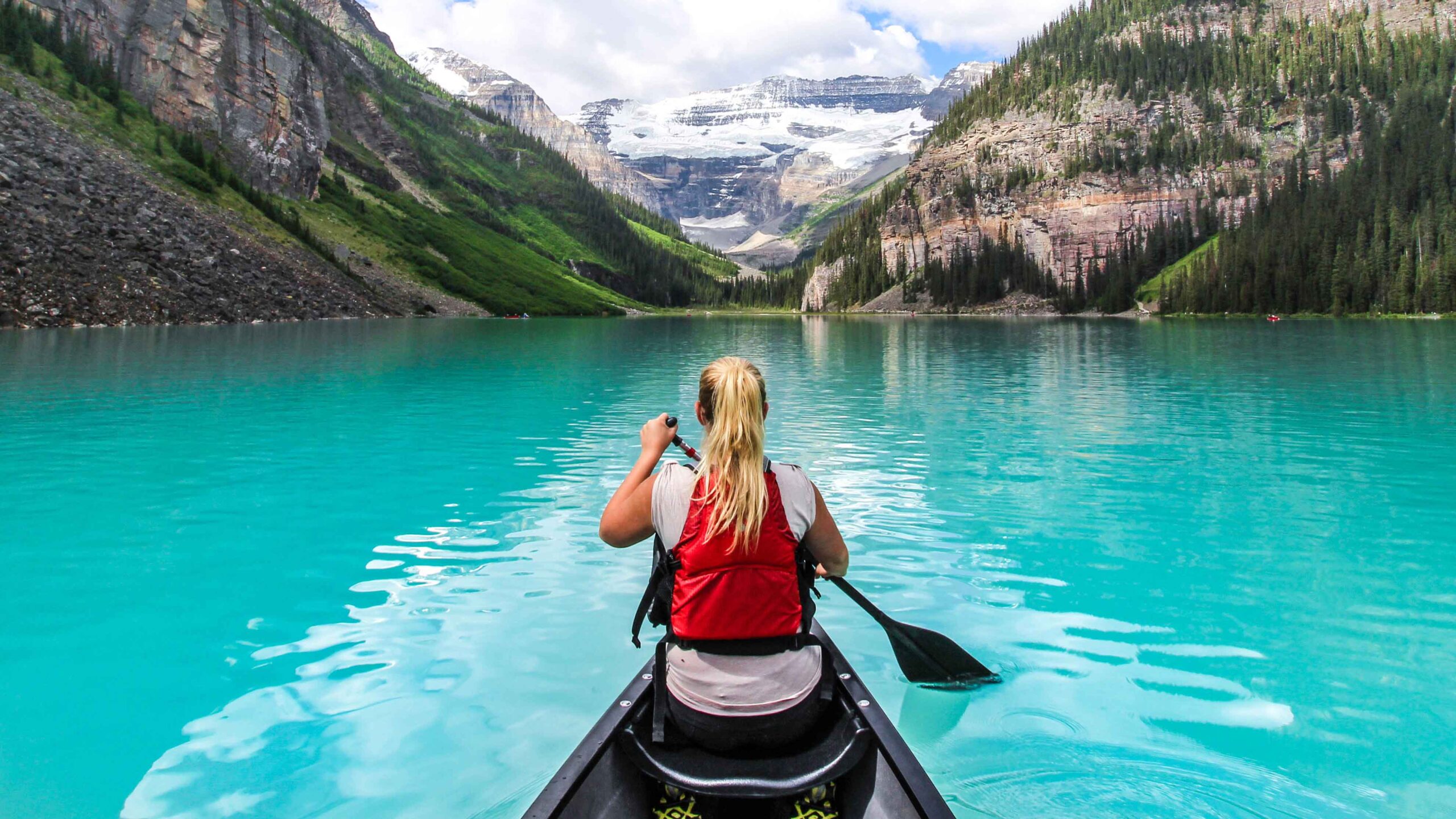 A woman canoes on Lake Louise wearing a red life jacket
