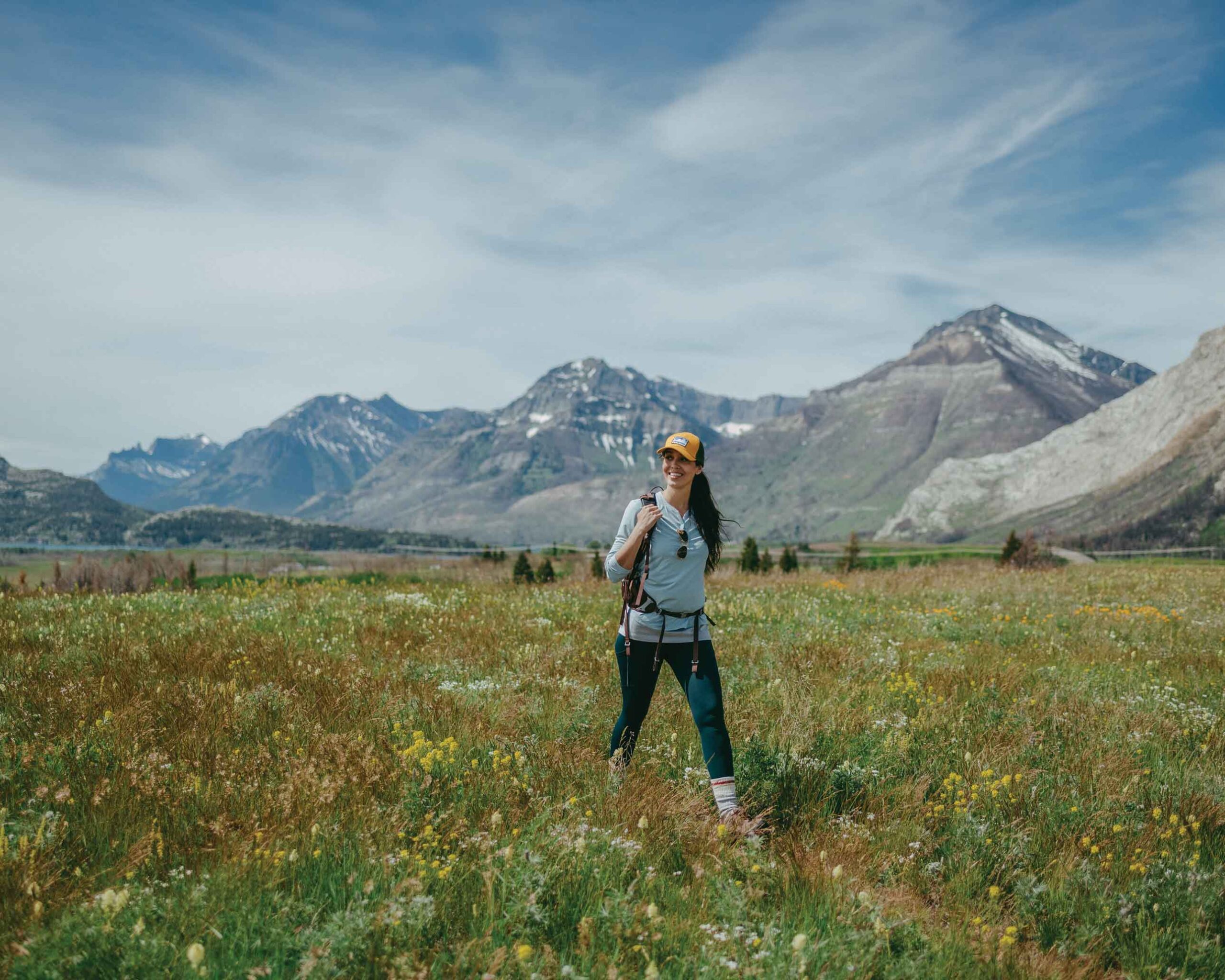 A woman walks through a field of wildflowers in Waterton Lakes National Park with mountains in the background